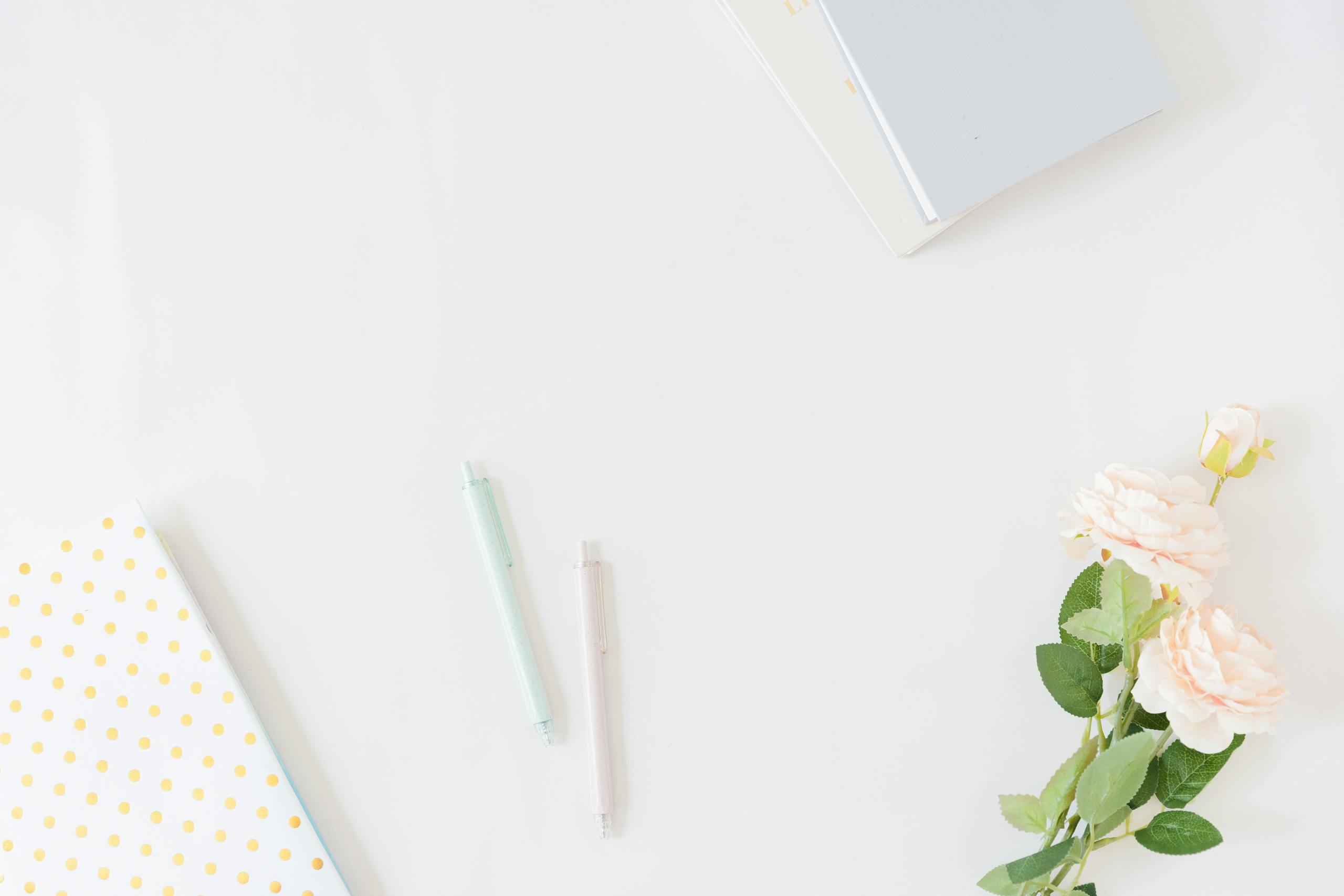 A clean and simple flat lay of notebooks, pens, and flowers on a white background.